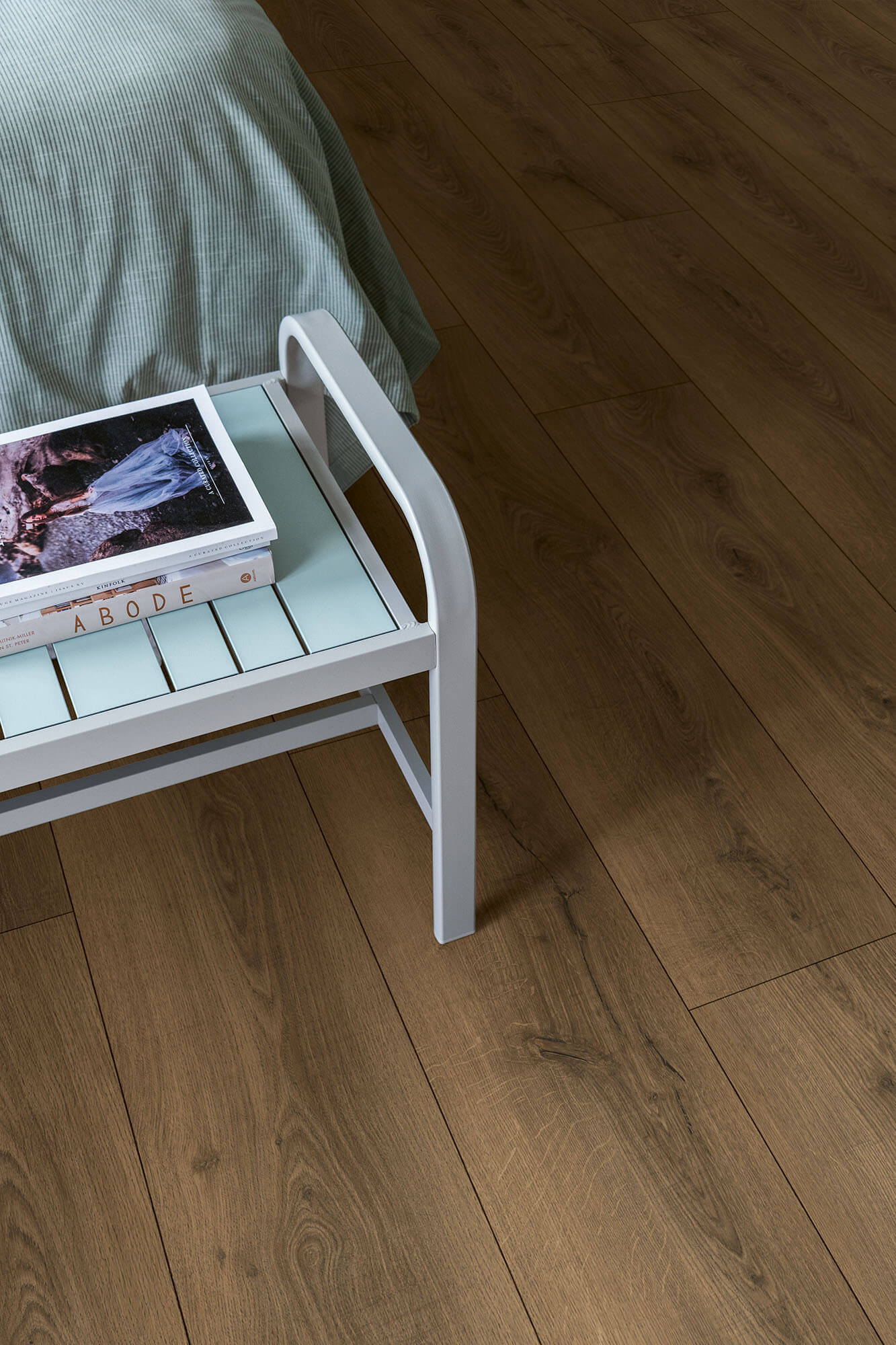 Small white side table with a green surface next to a bed on a wooden floor.