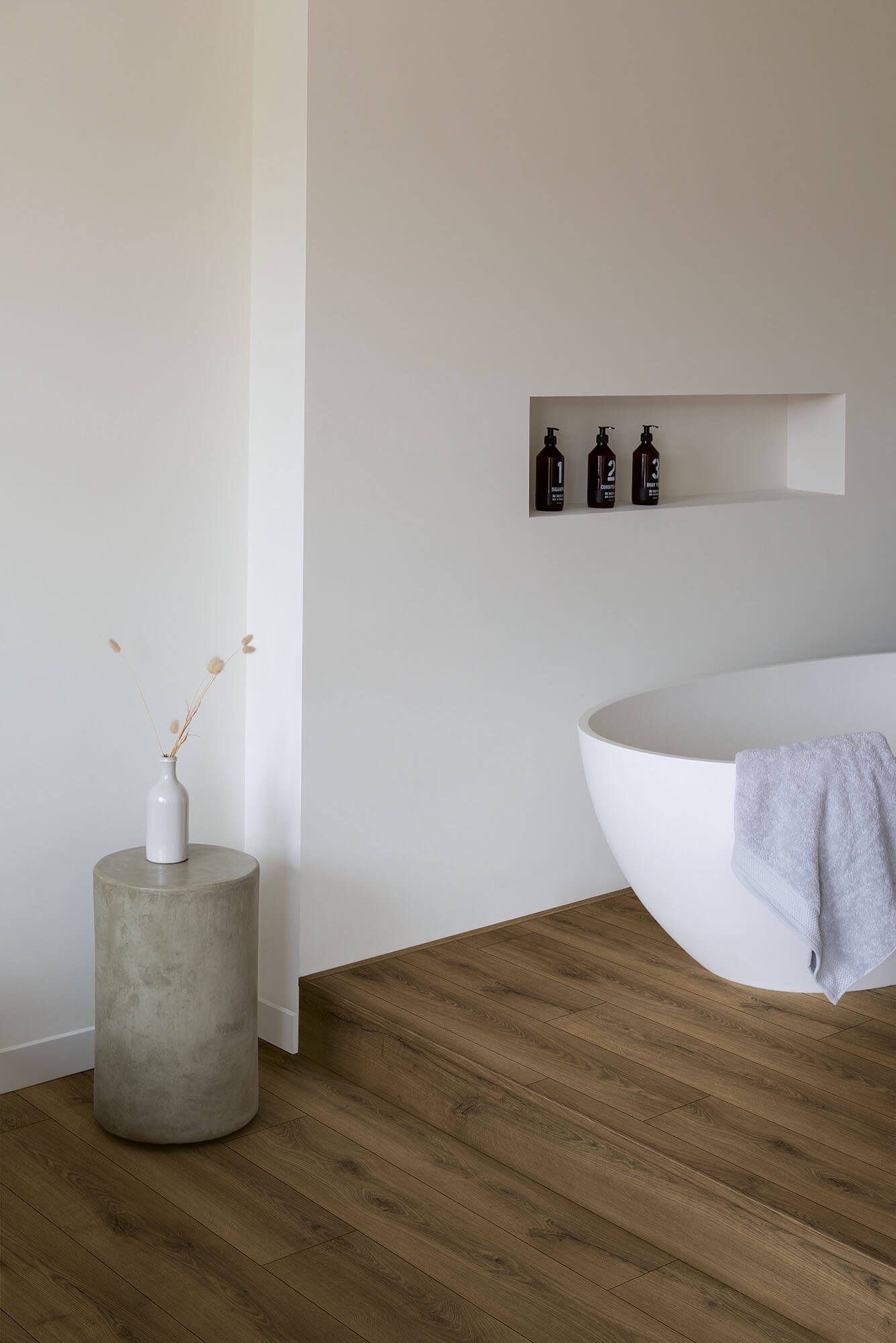 Modern bathroom with a white bathtub, concrete side table, and wall niches.