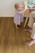 Child standing on a wooden floor with an adult's hand, possibly teaching or guiding them.