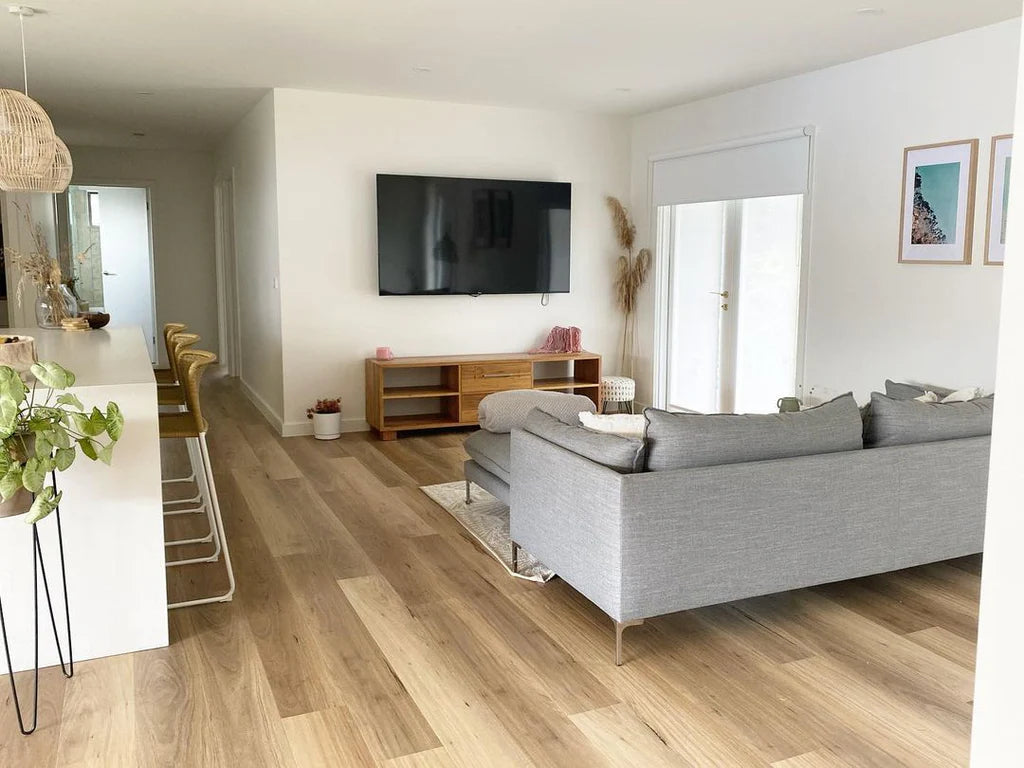 Modern living room with gray sofa, TV, and wooden floor.