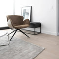 Modern brown chair in a minimalistic room with a rug and side table.