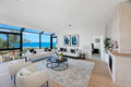 Modern living room with white furniture, large windows, and a view of the ocean.