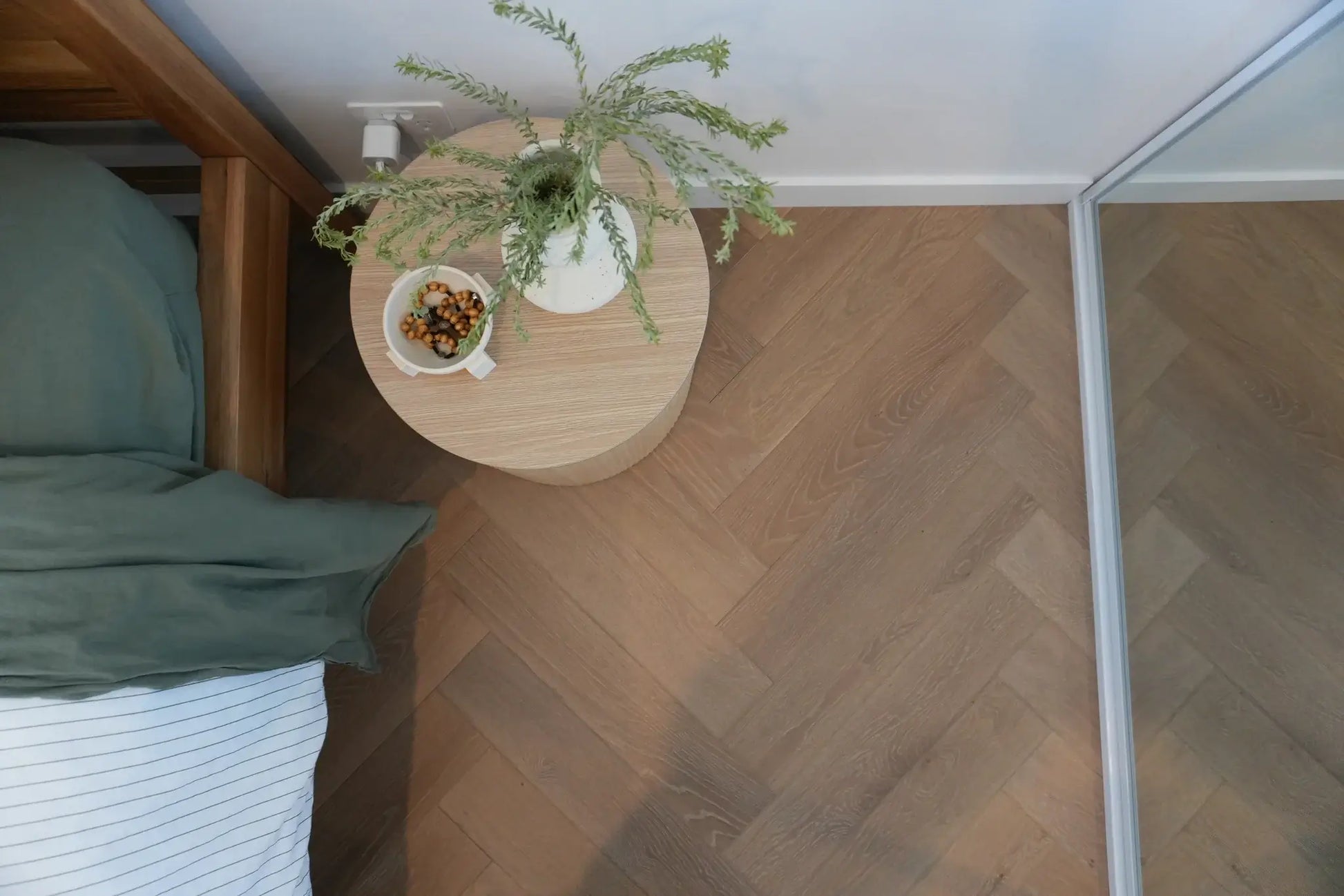 Small round table with a plant and bowl on a wooden floor next to a bed.