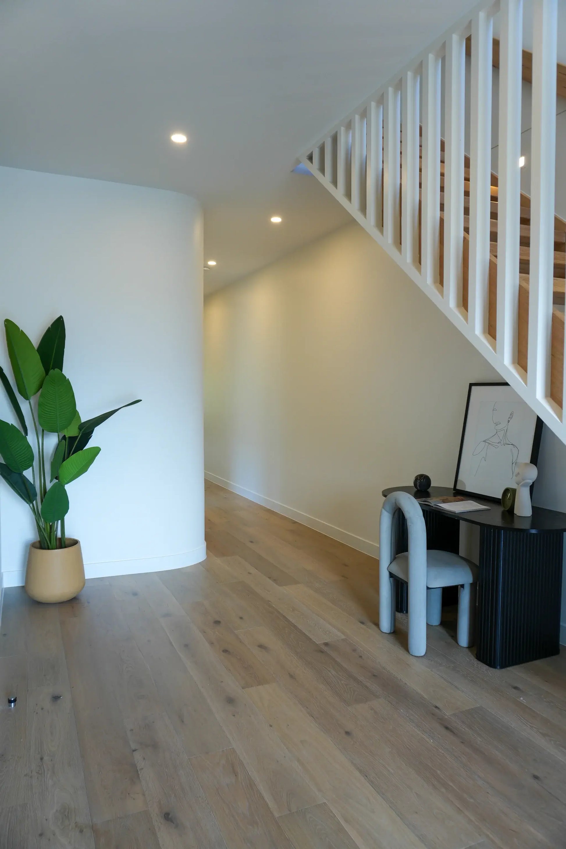 Modern interior with a staircase, desk, and plant on a wooden floor.