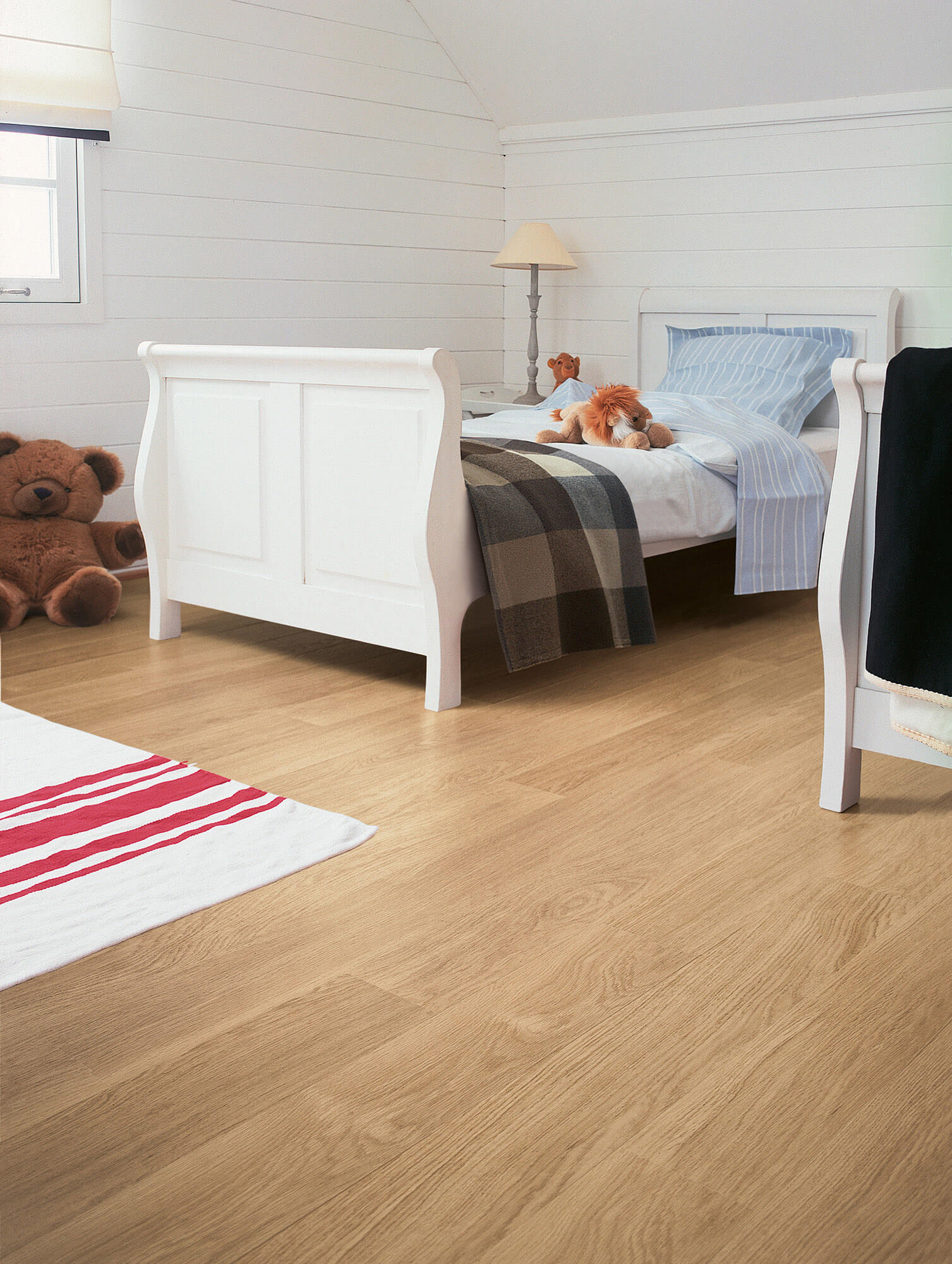 Children's bedroom with white sleigh bed, teddy bears, and wooden flooring.