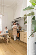 Two women in a modern kitchen with wooden floors and white walls.
