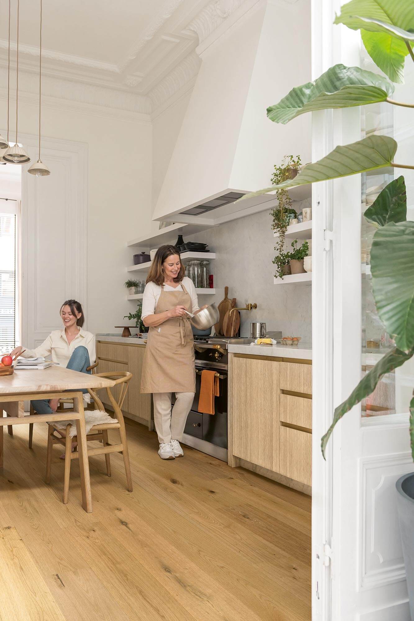 Two women in a modern kitchen with wooden floors and white walls.