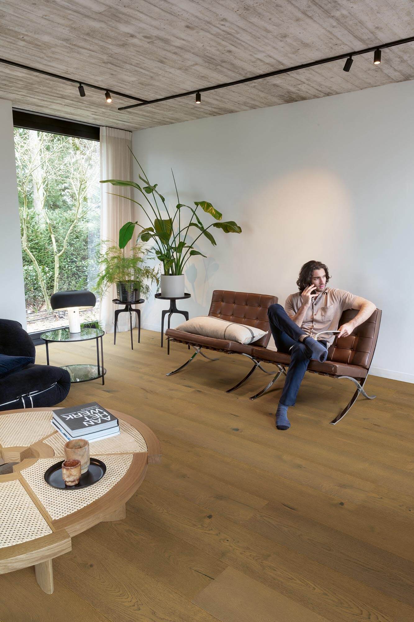 Person sitting on a brown leather chair in a modern living room with large windows and wooden flooring.