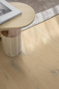 Wooden side table with a cylindrical base on a wooden floor.