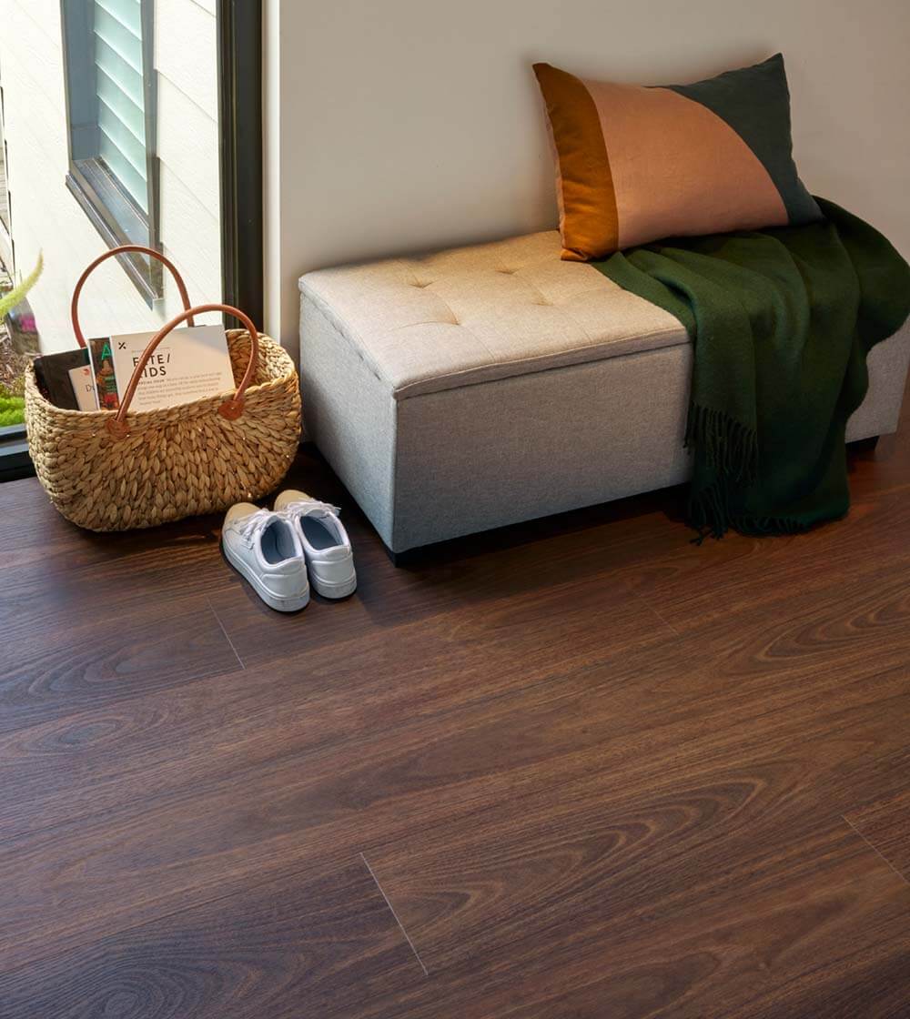 Gray ottoman with pillows and a basket on a wooden floor