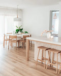 Modern kitchen with wooden dining table and stools, white countertops, and pendant lights.