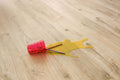 Red paint roller with yellow paint spill on a wooden floor