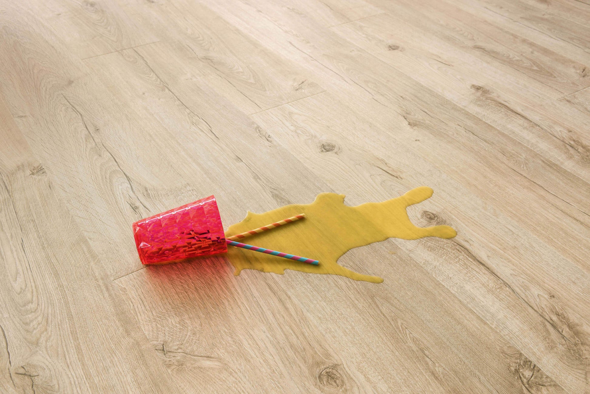 Red paint roller with yellow paint spill on a wooden floor