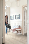 Woman holding an umbrella in a bright, minimalistic room with white walls and wooden floors.