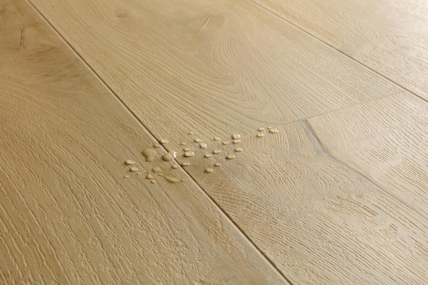 Light oak wood flooring planks with visible grain and a small spill of water and debris near the center.