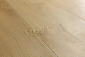 Light oak wood flooring planks with visible grain and a small spill of water and debris near the center.