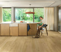 Woman sitting on a stool in a modern kitchen with a dog, surrounded by large windows with a view of greenery.