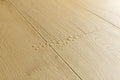 Close-up of light oak wood flooring planks with visible grain texture and a few water droplets on the surface.