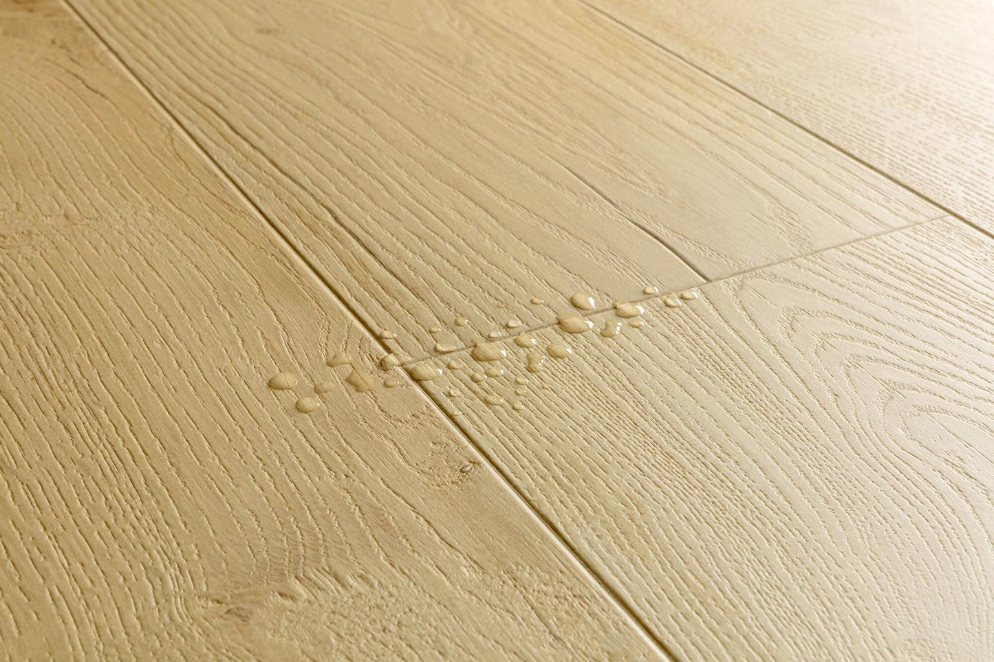 Close-up of light oak wood flooring planks with visible grain texture and a few water droplets on the surface.