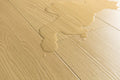 Close-up of light beige wood-look flooring with a glossy liquid spill running across the surface.