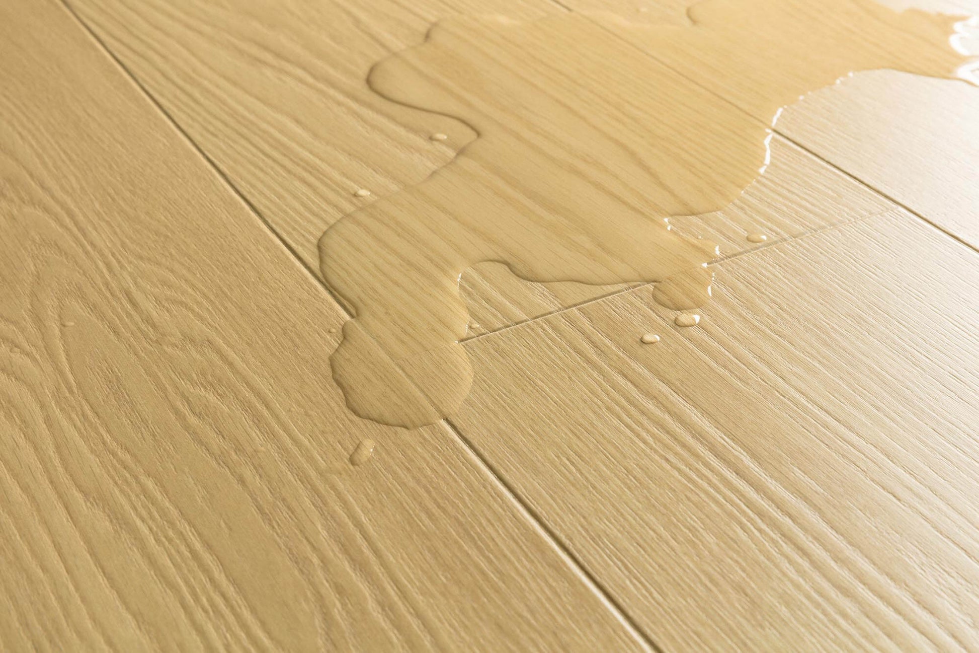 Close-up of light beige wood-look flooring with a glossy liquid spill running across the surface.