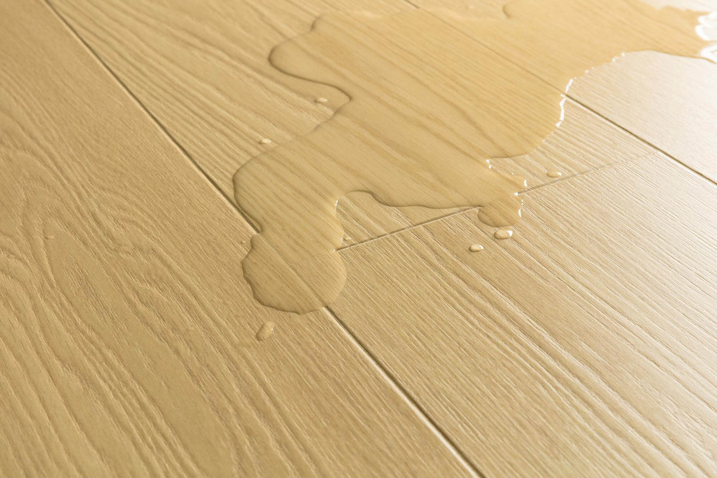 Close-up of light beige wood-look flooring with a glossy liquid spill running across the surface.