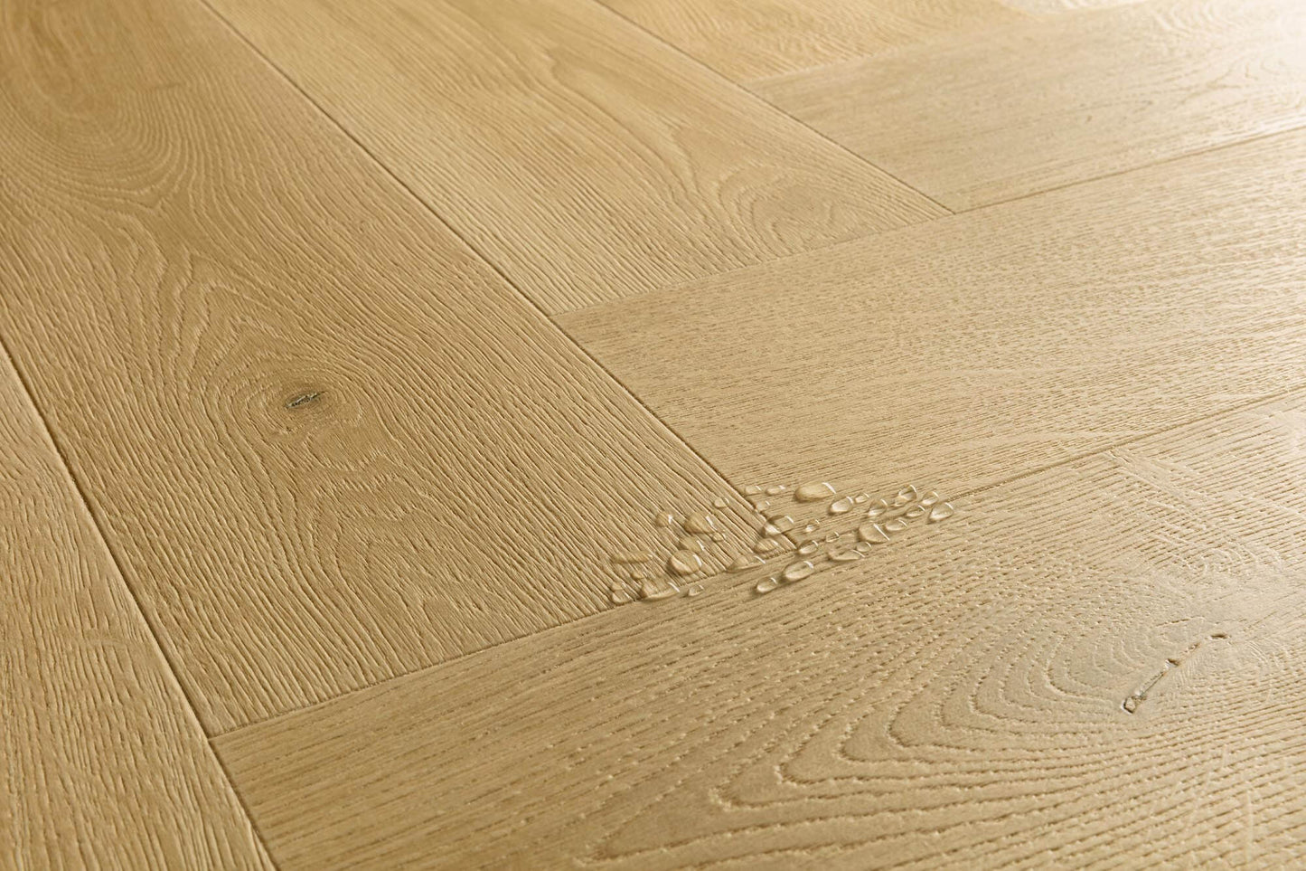 Light oak wood flooring planks arranged in a herringbone pattern, showing natural wood grain and a small cluster of water droplets on one plank.