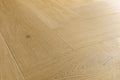 Light oak wood flooring planks arranged in a herringbone pattern, showing natural wood grain and subtle knots.
