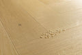 Light oak wood flooring planks arranged in a herringbone pattern, with a small cluster of broken glass chips on the surface.