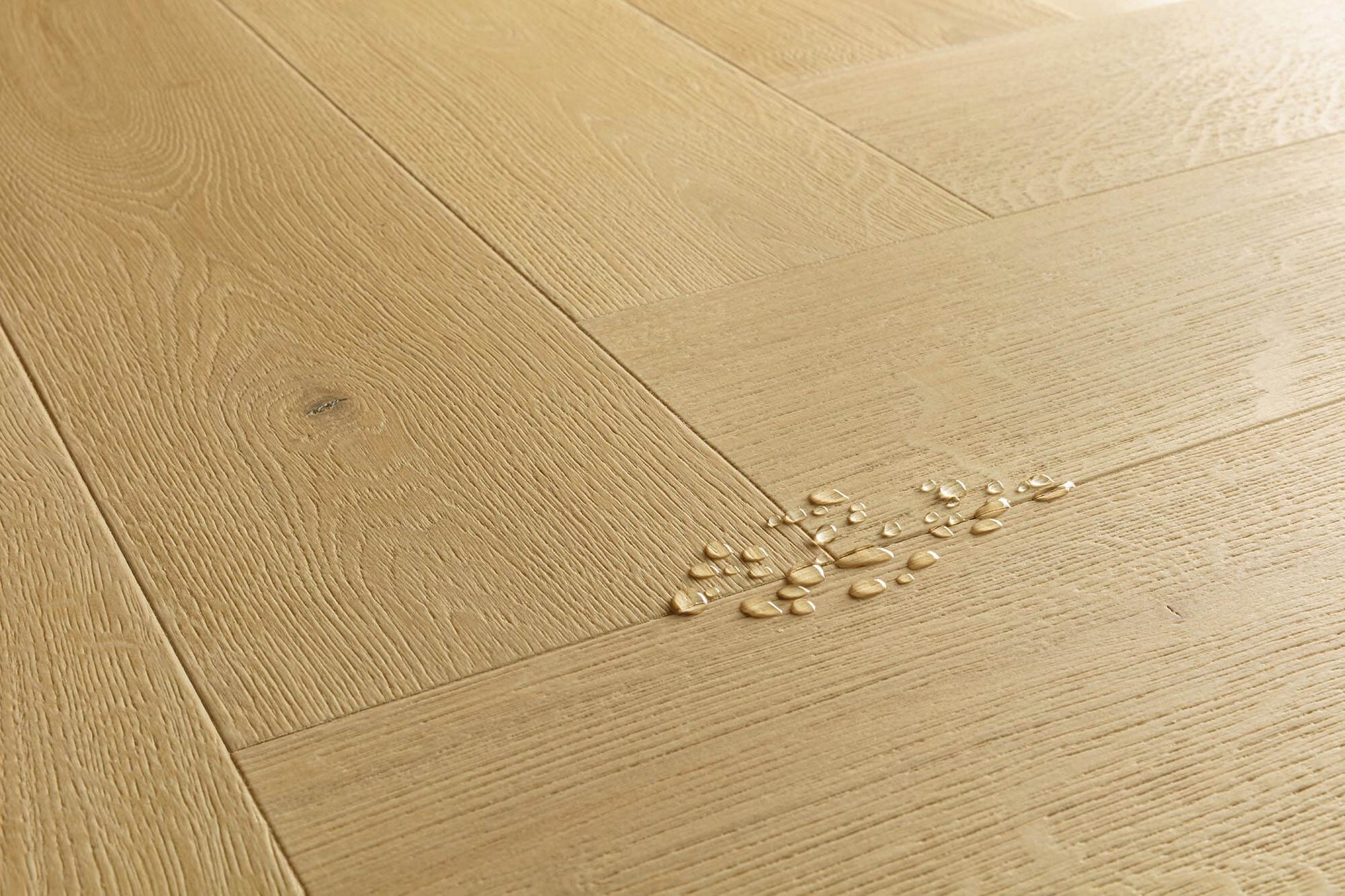 Light oak wood flooring planks arranged in a herringbone pattern, with a small cluster of broken glass chips on the surface.