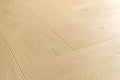 Light natural oak wood flooring planks arranged in a herringbone pattern, showing detailed wood grain and subtle knots.