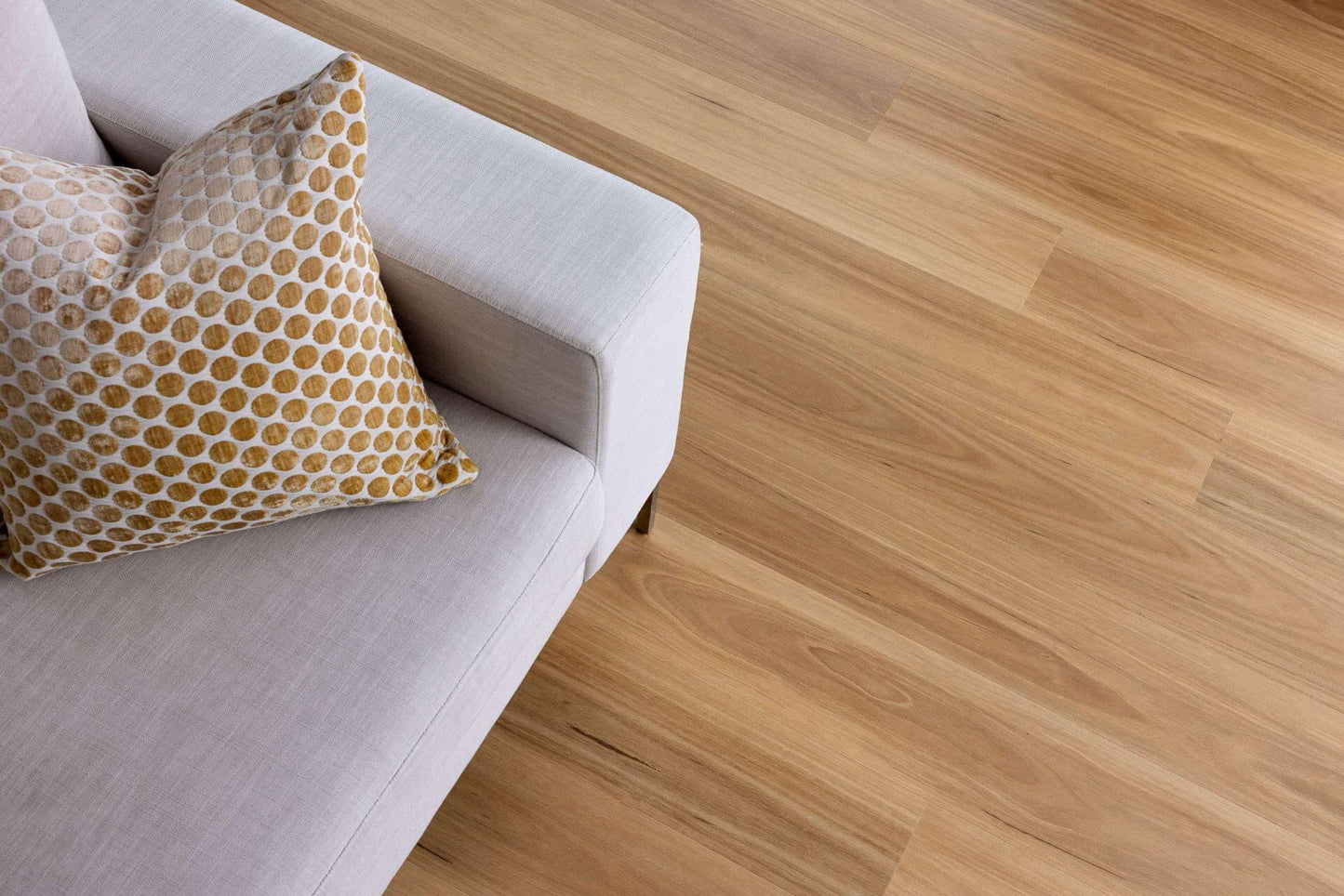 Light oak wood plank flooring shown in a modern living room setting next to a light gray sofa with a patterned throw pillow.