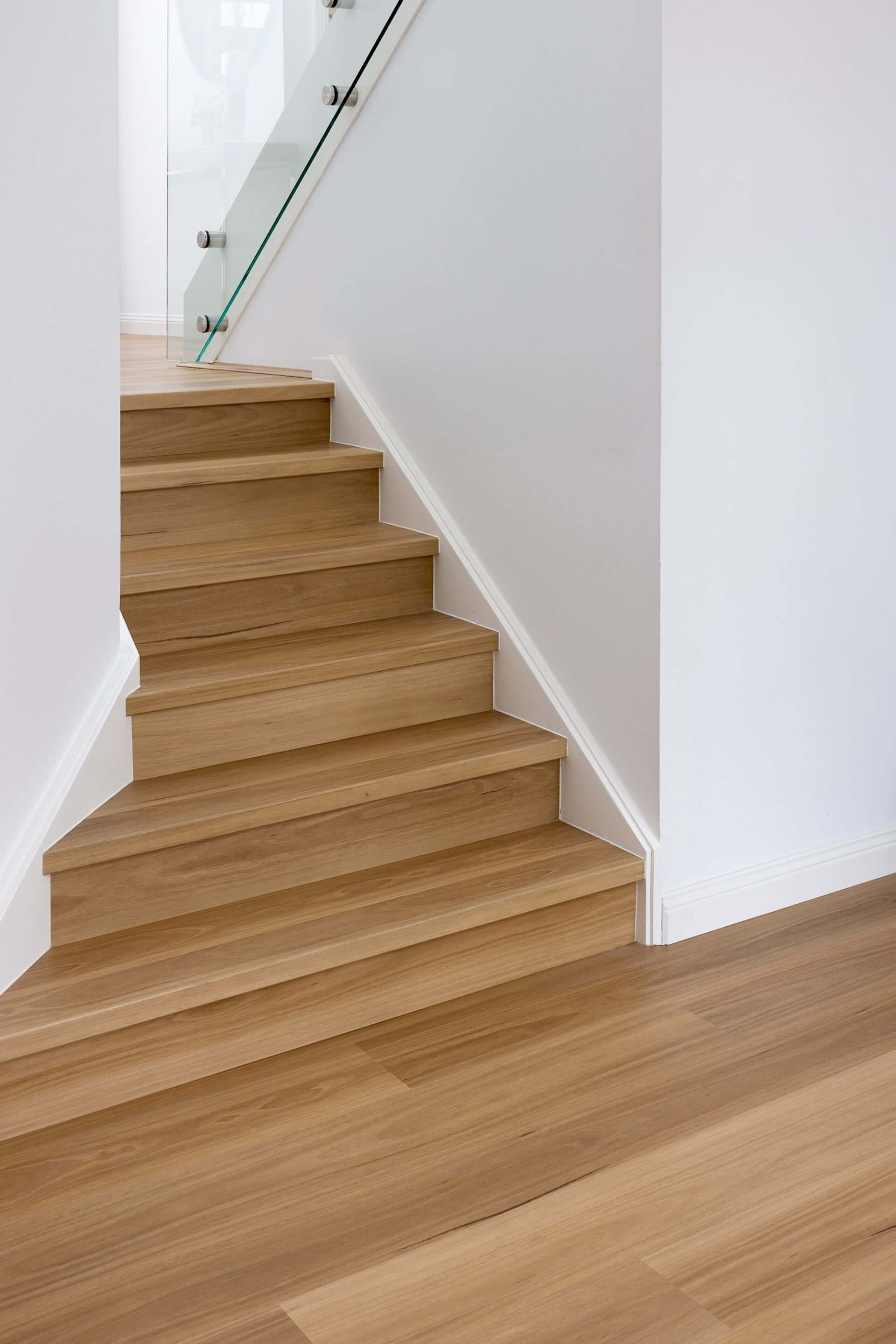 Light oak wood staircase steps with a glass railing and white walls in a modern interior setting.