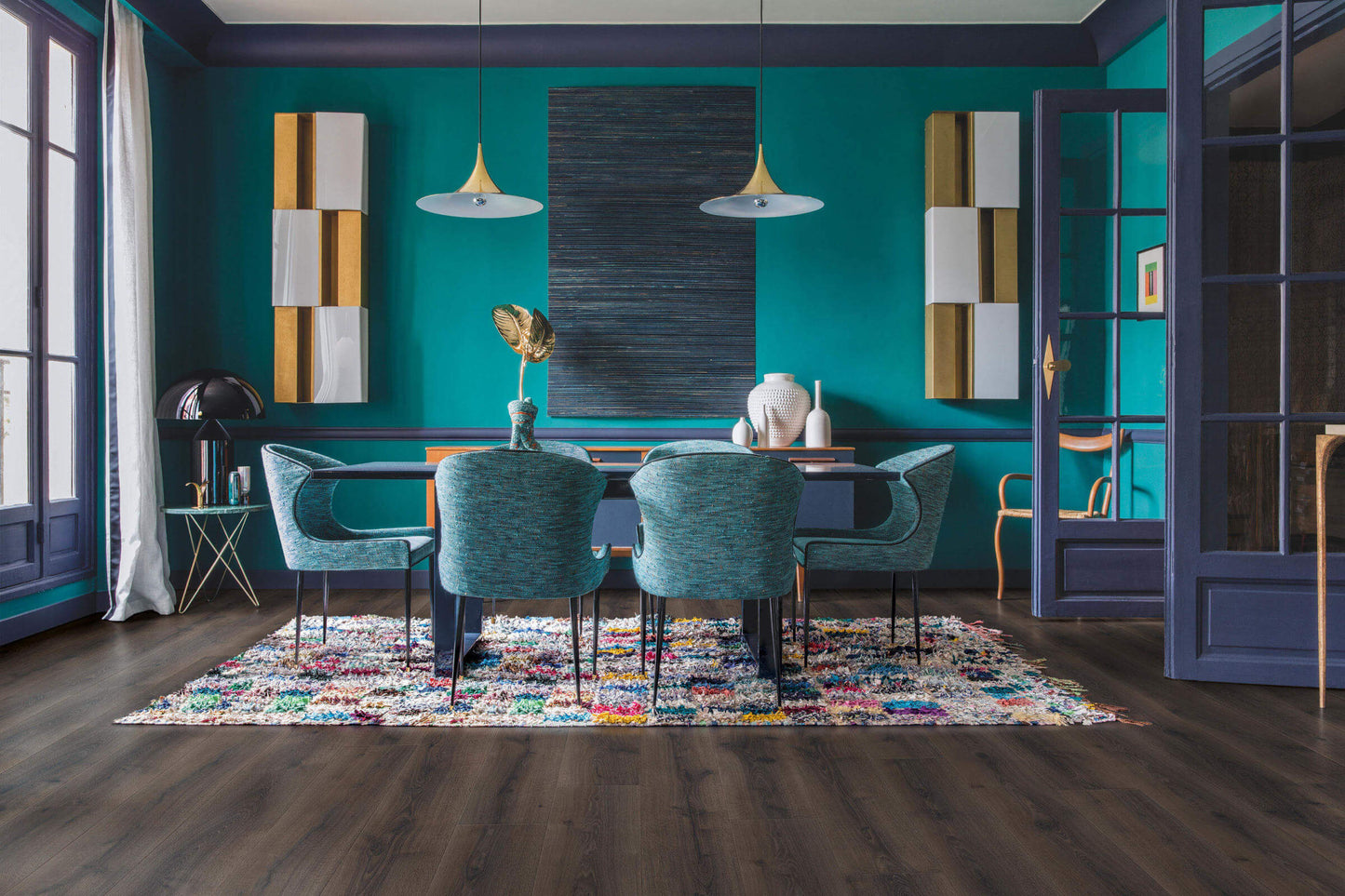 Modern dining room with teal walls, colorful rug, and stylish furniture.