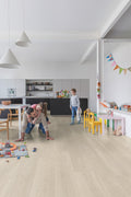 Family playing on a light wood floor in a modern kitchen and living area.