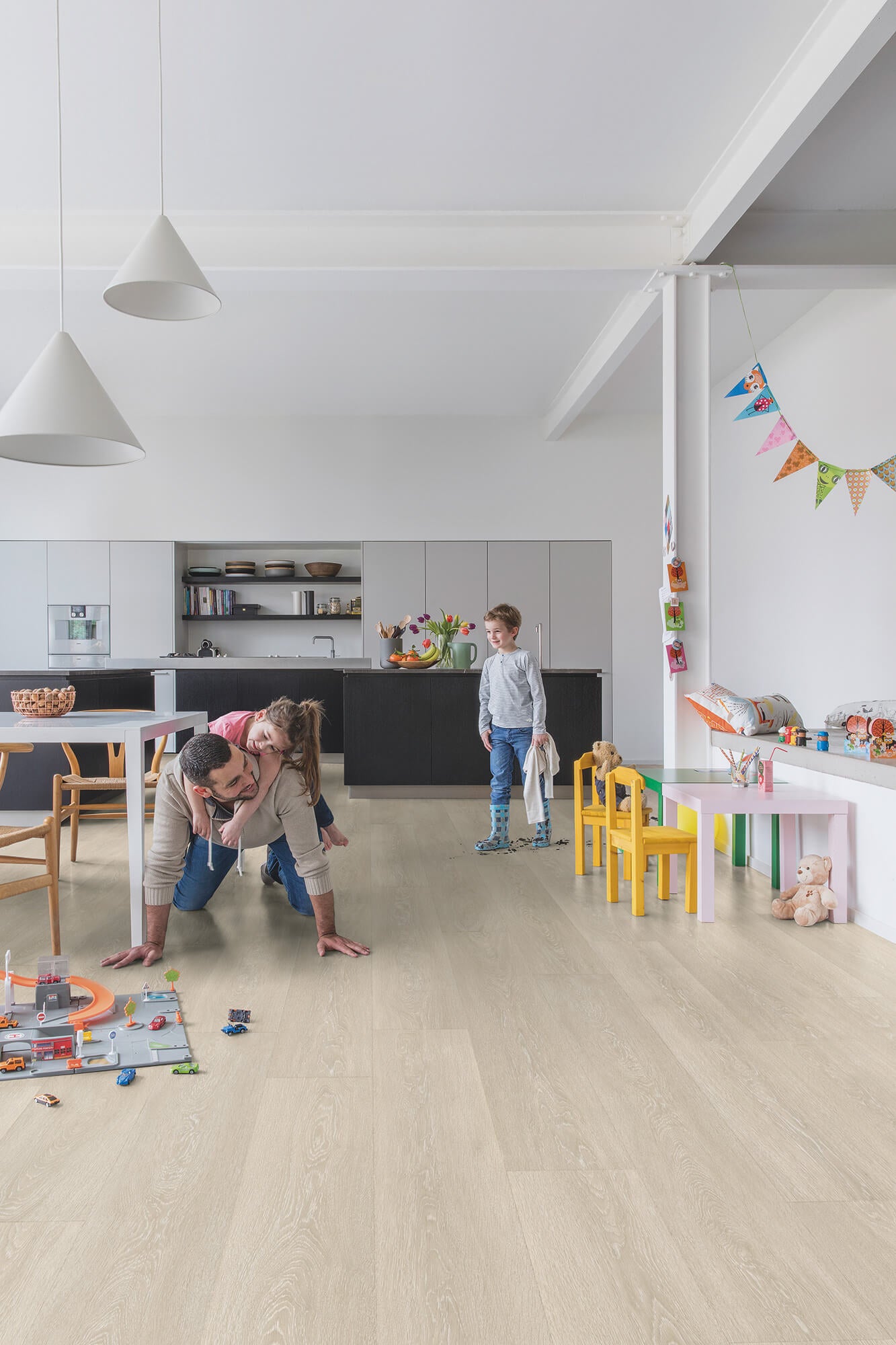 Family playing on a light wood floor in a modern kitchen and living area.