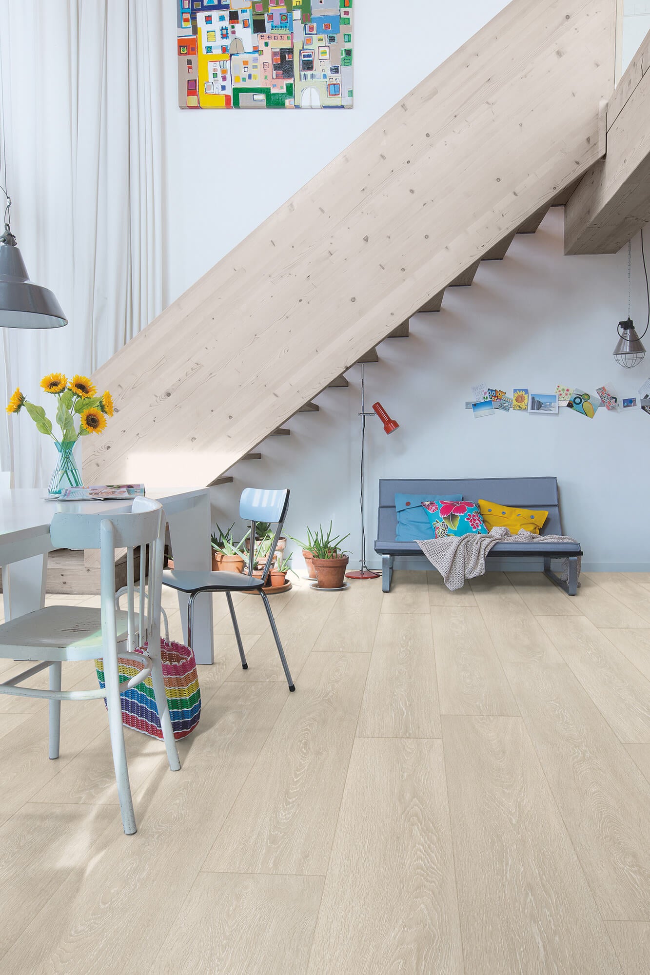 Modern living room with light wood flooring, staircase, and colorful decor.