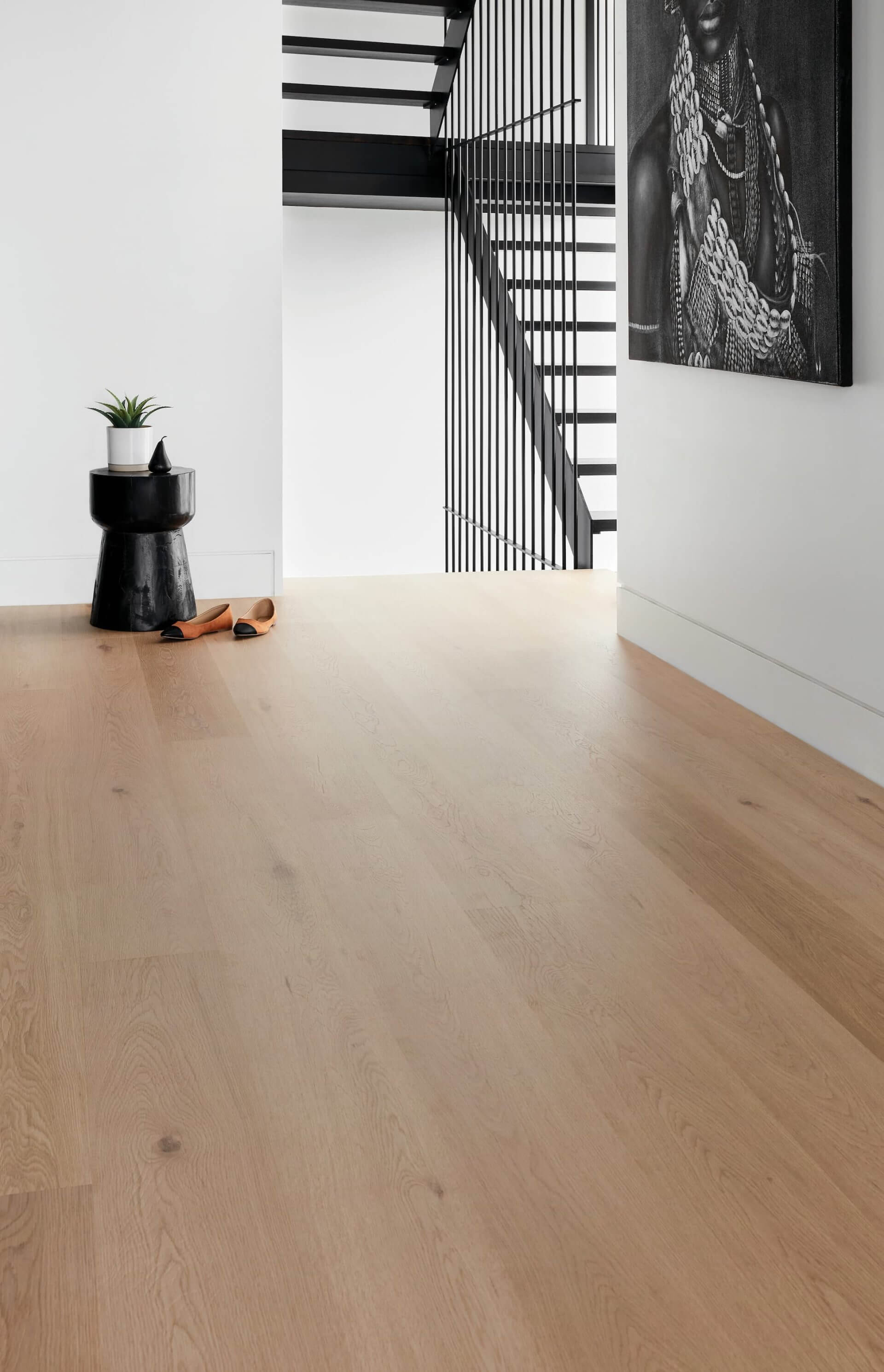 Modern interior with wooden floor, black staircase, and artwork on white wall.