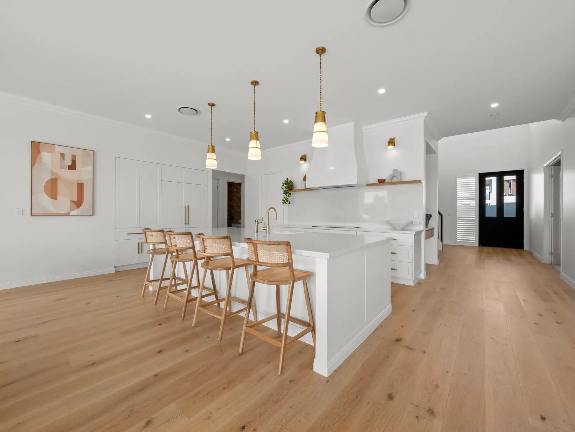 Modern kitchen with white island, wooden chairs, and pendant lights.