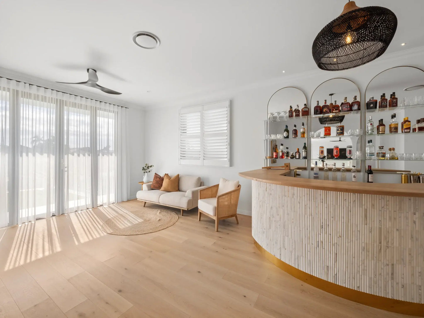 Modern living room with a bar area featuring shelves of bottles.