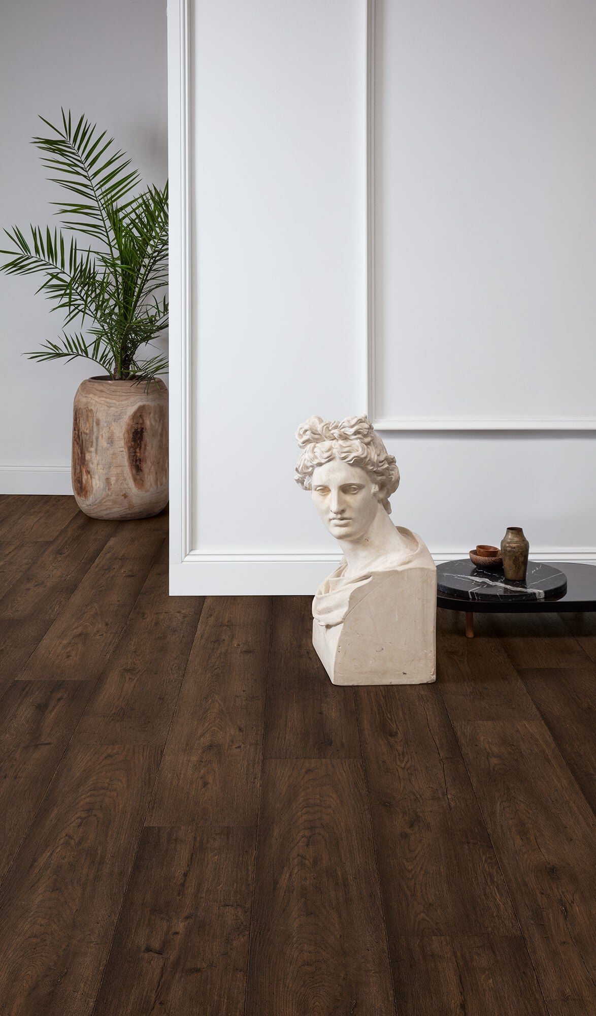 Bust sculpture on a wooden floor with a plant and decorative items in the background