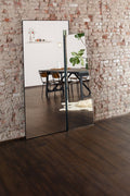 Full-length mirror leaning against a brick wall reflecting a dining area.