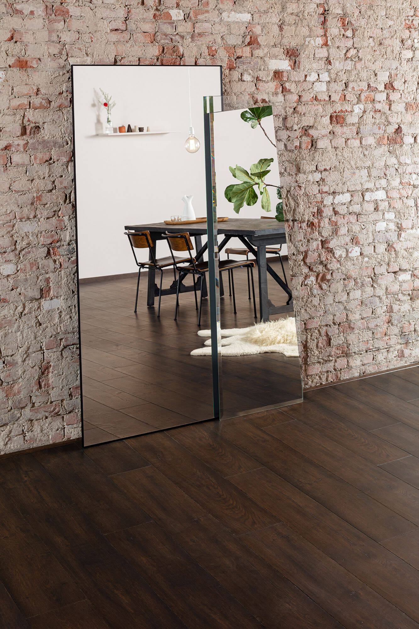 Full-length mirror leaning against a brick wall reflecting a dining area.