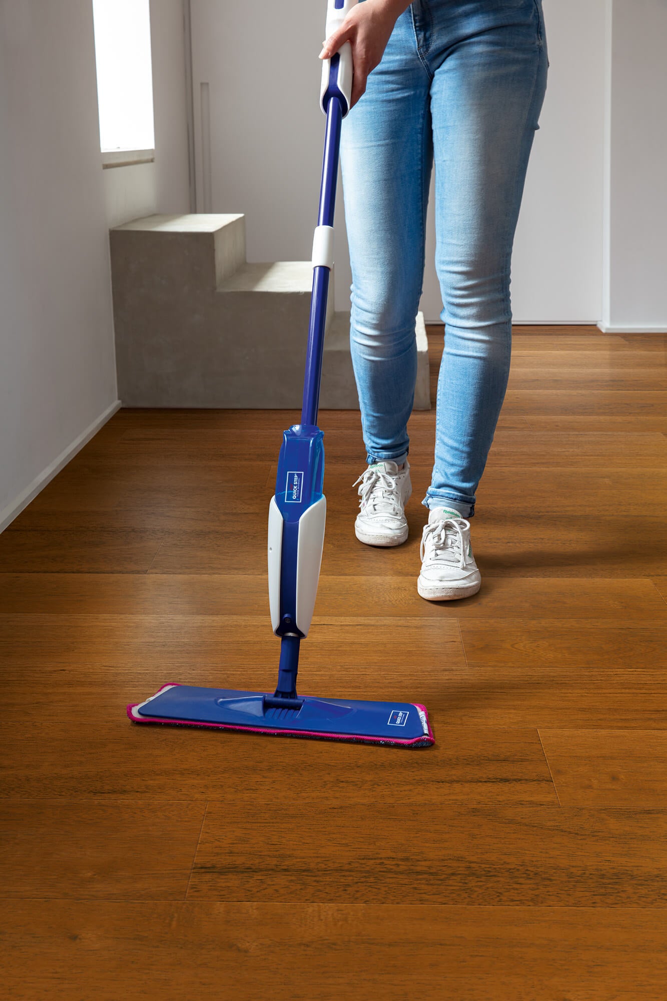Person using a blue and white spray mop on a wooden floor.