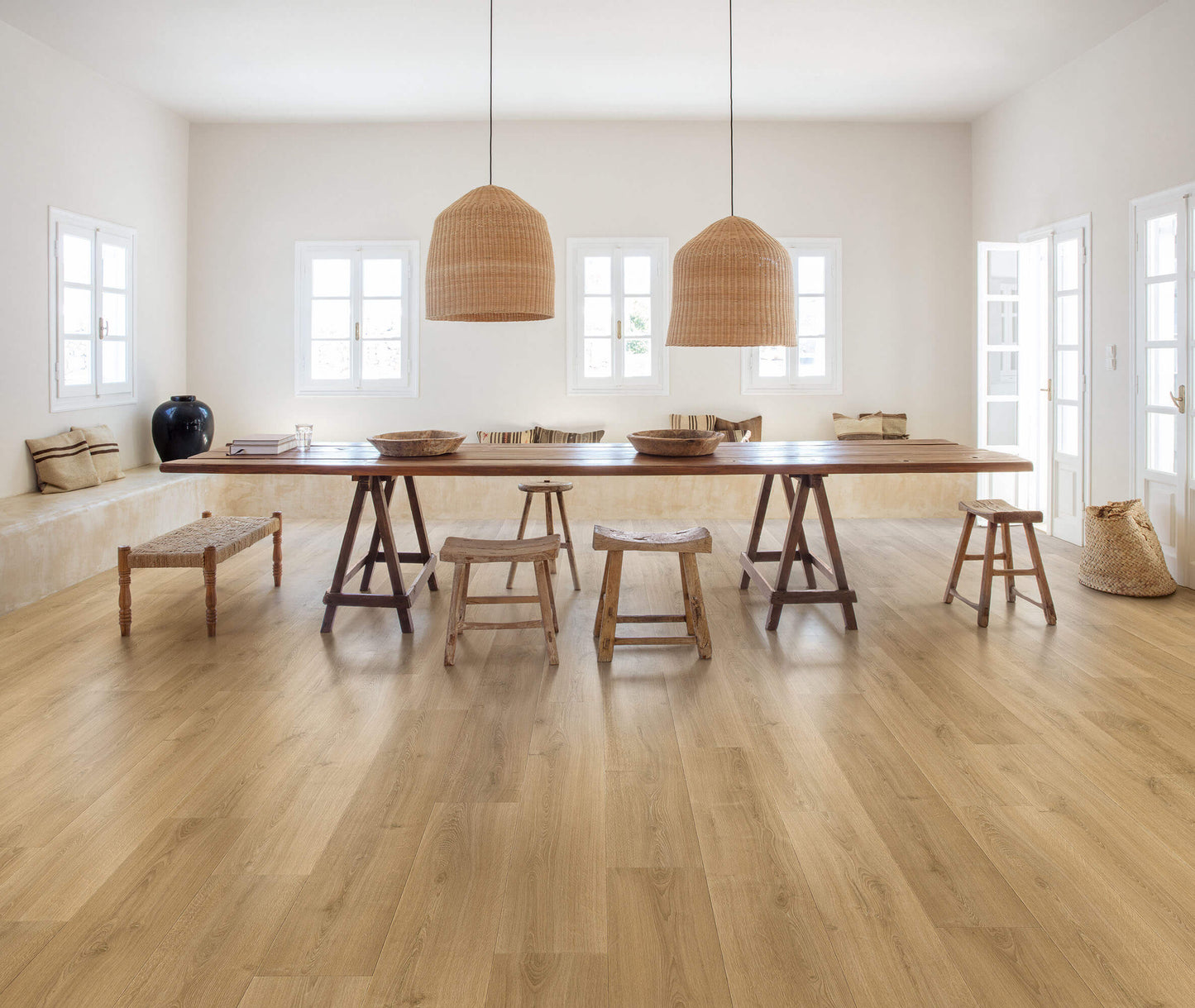 Wooden dining table with stools in a bright room with large windows.