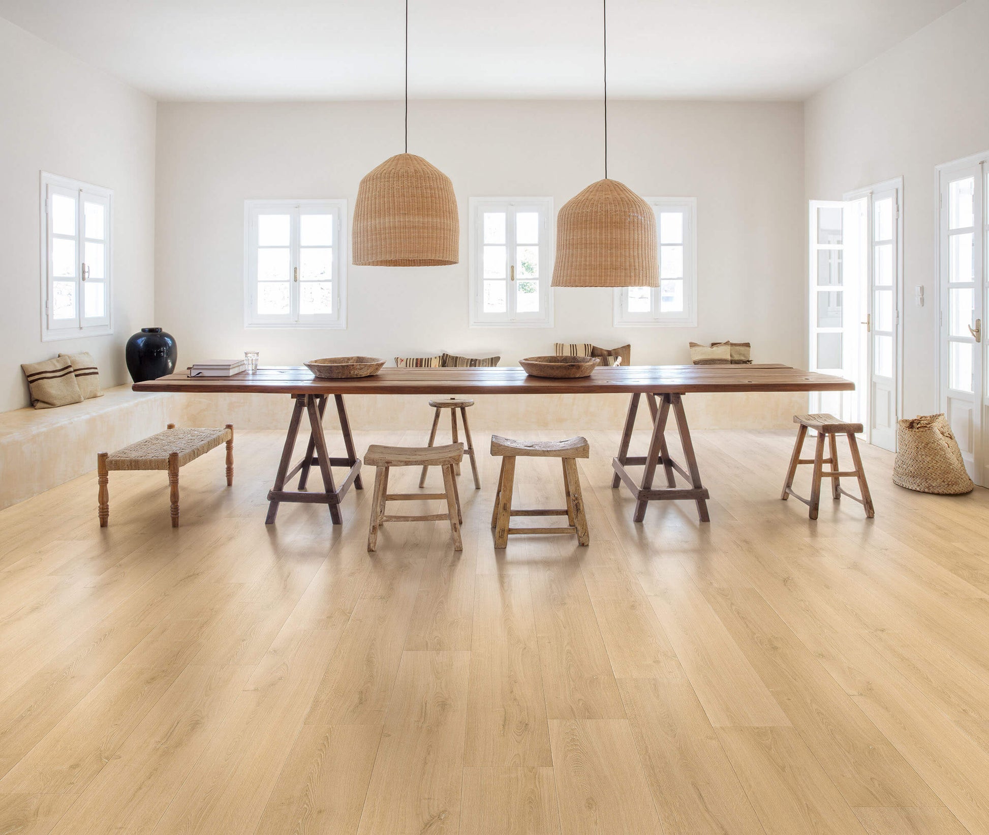 Dining area with a long wooden table and stools in a bright room.