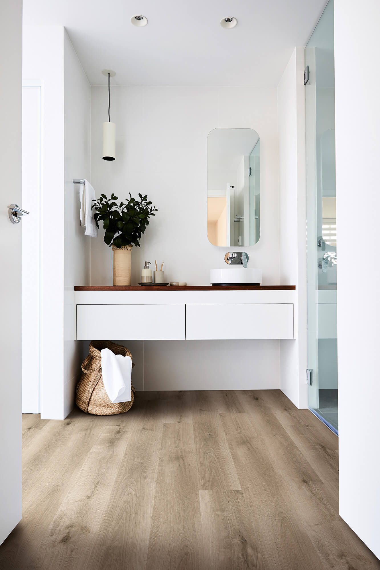 Modern bathroom with wooden vanity, mirror, and plant.