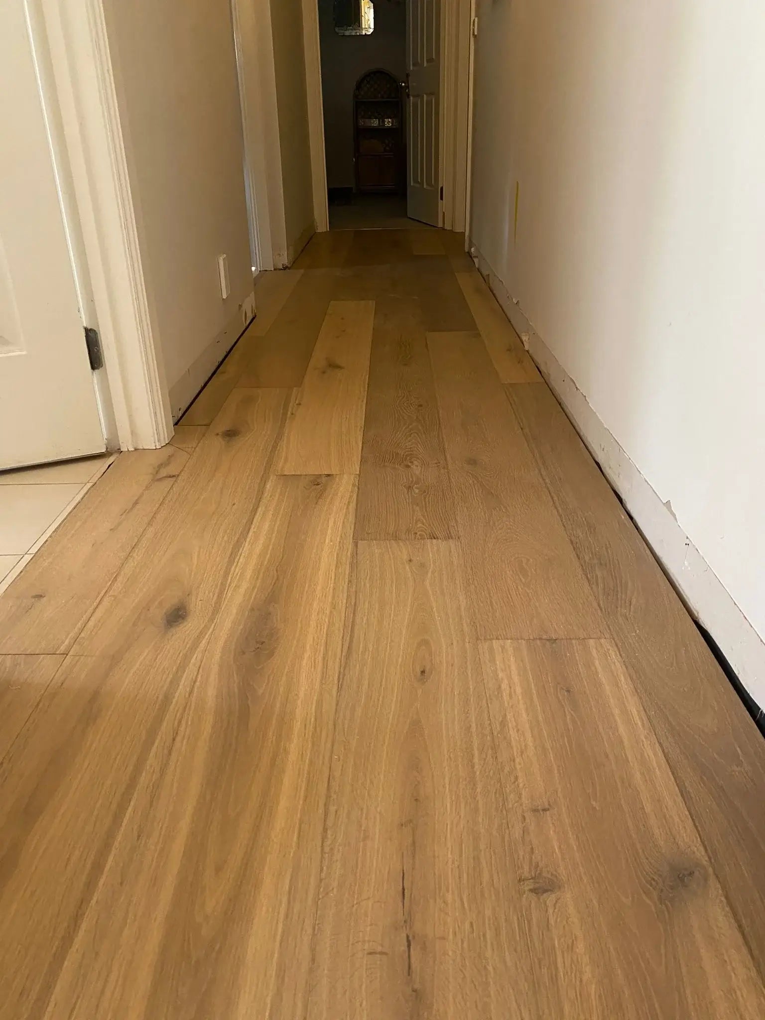 Wooden flooring in a hallway with white walls and baseboards.