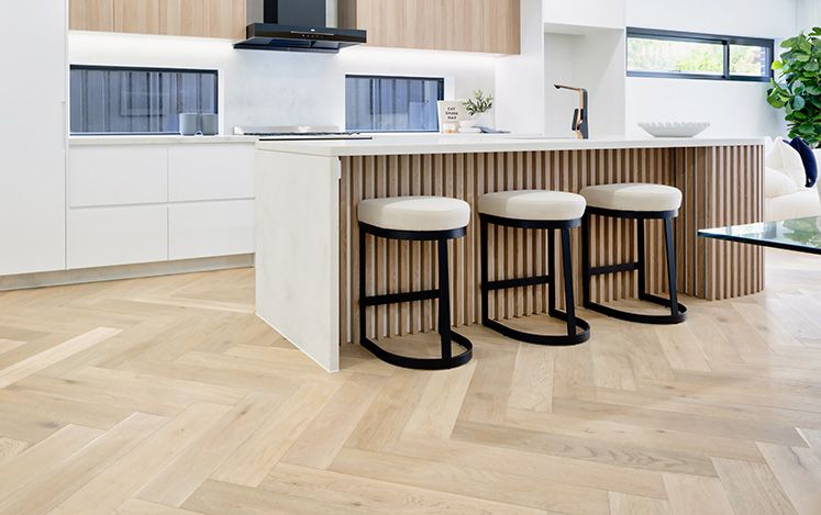 Modern kitchen with white island, stools, and wooden flooring.
