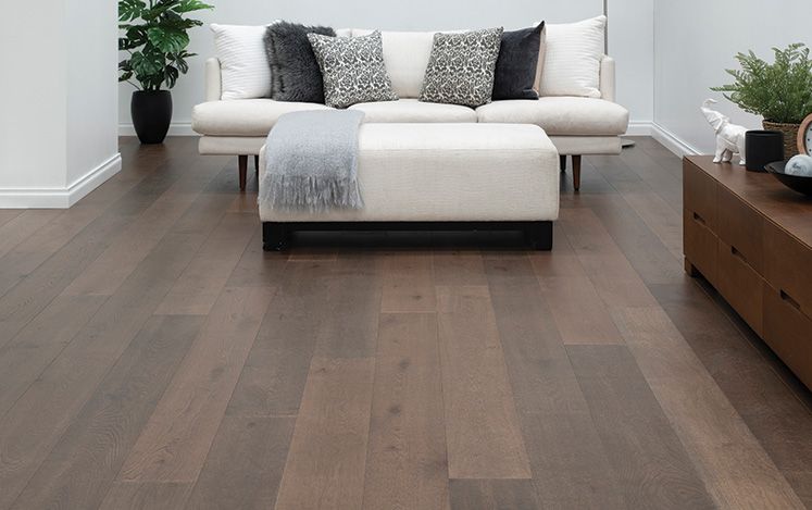 Living room with a beige sofa, ottoman, and decorative pillows on a wooden floor.